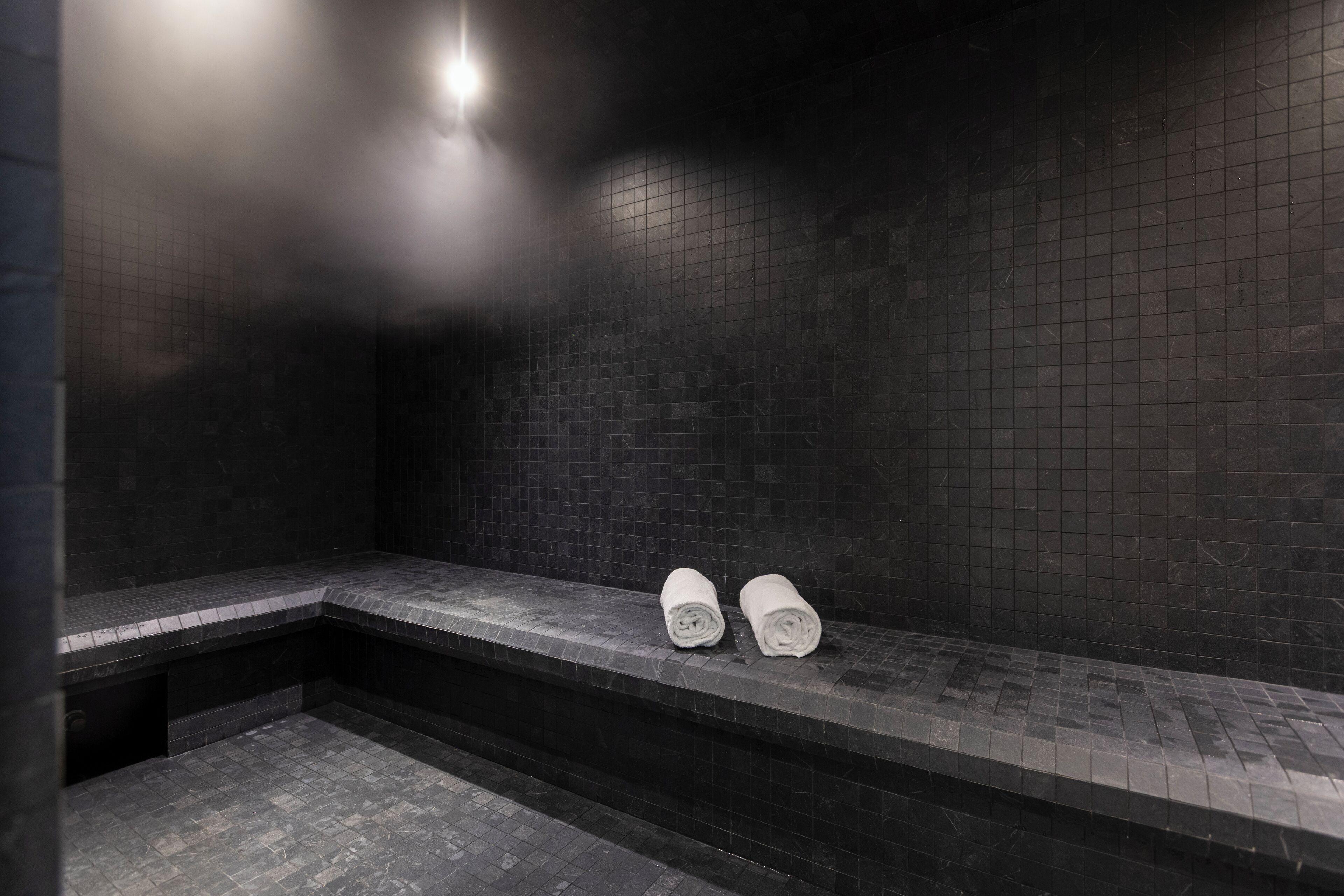 Un baño oscuro con baldosas, un banco y dos toallas enrolladas.
