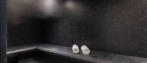 Un baño oscuro con baldosas, un banco y dos toallas enrolladas.