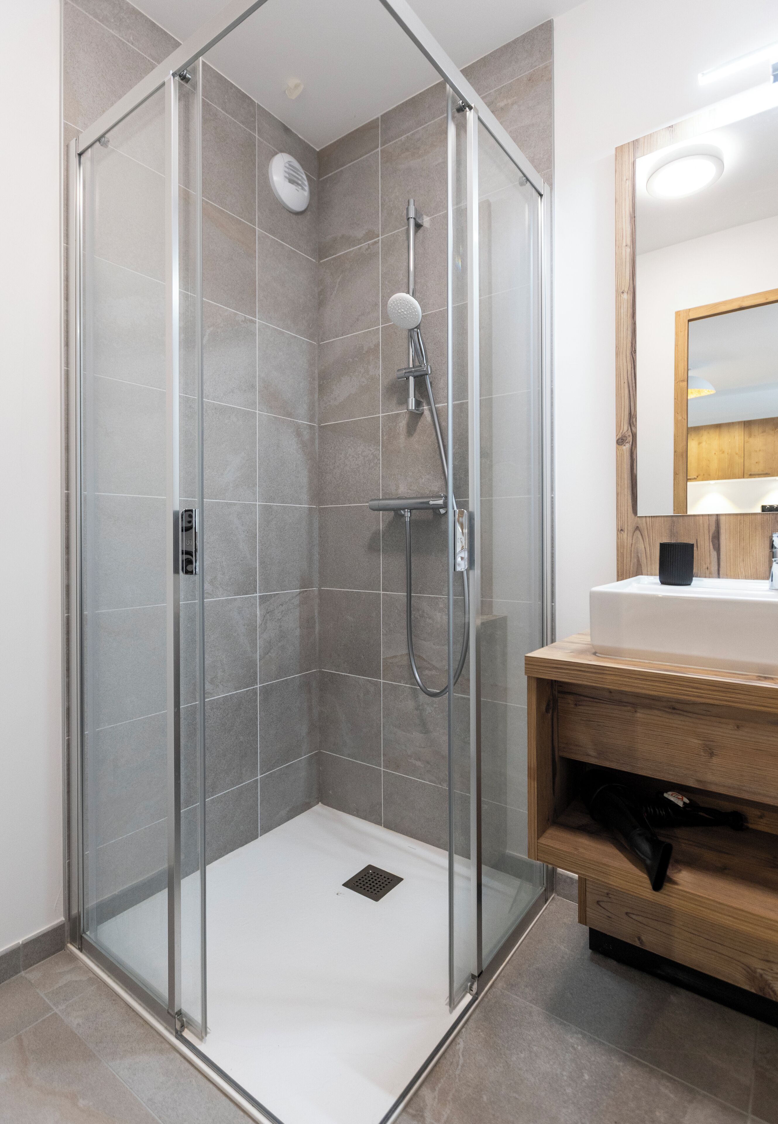 Un bagno moderno con doccia vetrata, un mobile lavabo in legno e uno specchio grande.