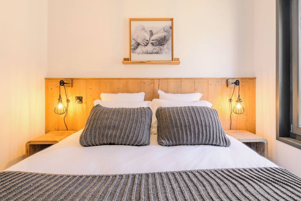A neatly made bed with two pillows and a blanket, wooden headboard, bedside lamps, and a framed picture on the wall.