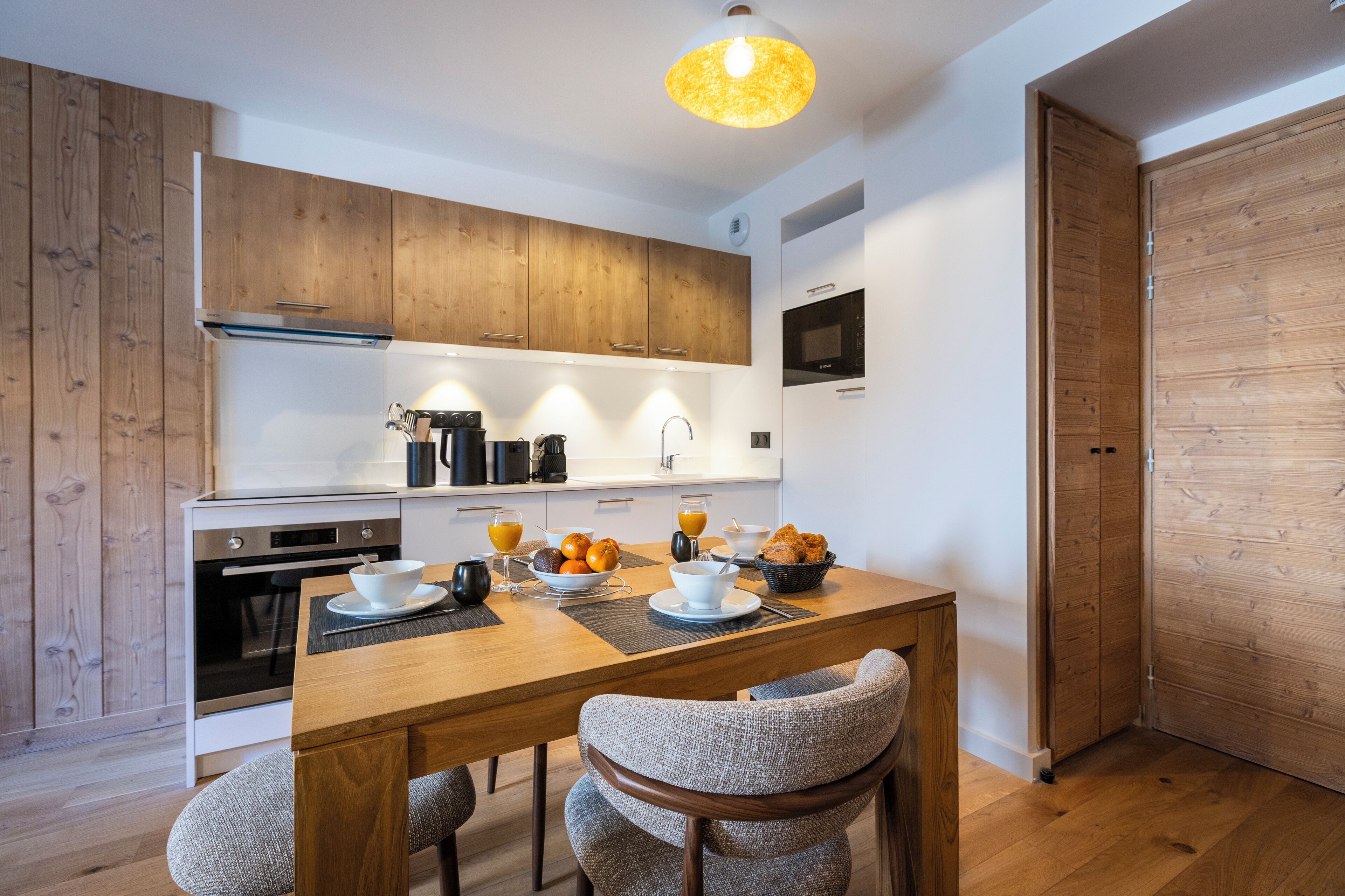 A modern kitchen with wooden cabinets, a dining table with chairs, and breakfast items.