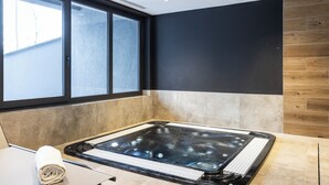 A modern spa room with a large hot tub, a window, and a wooden wall. - TERRESENS - Les Sources de Canopée  (Saint-Gervais-les-Bains)