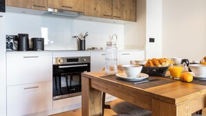 A modern kitchen with wooden cabinets, a built-in oven, and a breakfast setup including orange juice and croissants. - TERRESENS - Les Sources de Canopée  (Saint-Gervais-les-Bains)