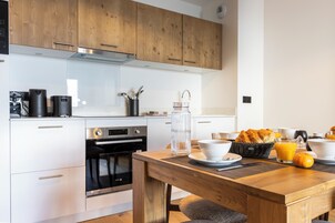 Una cocina moderna con armarios de madera, horno empotrado y una zona de desayuno con zumo de naranja y cruasanes.