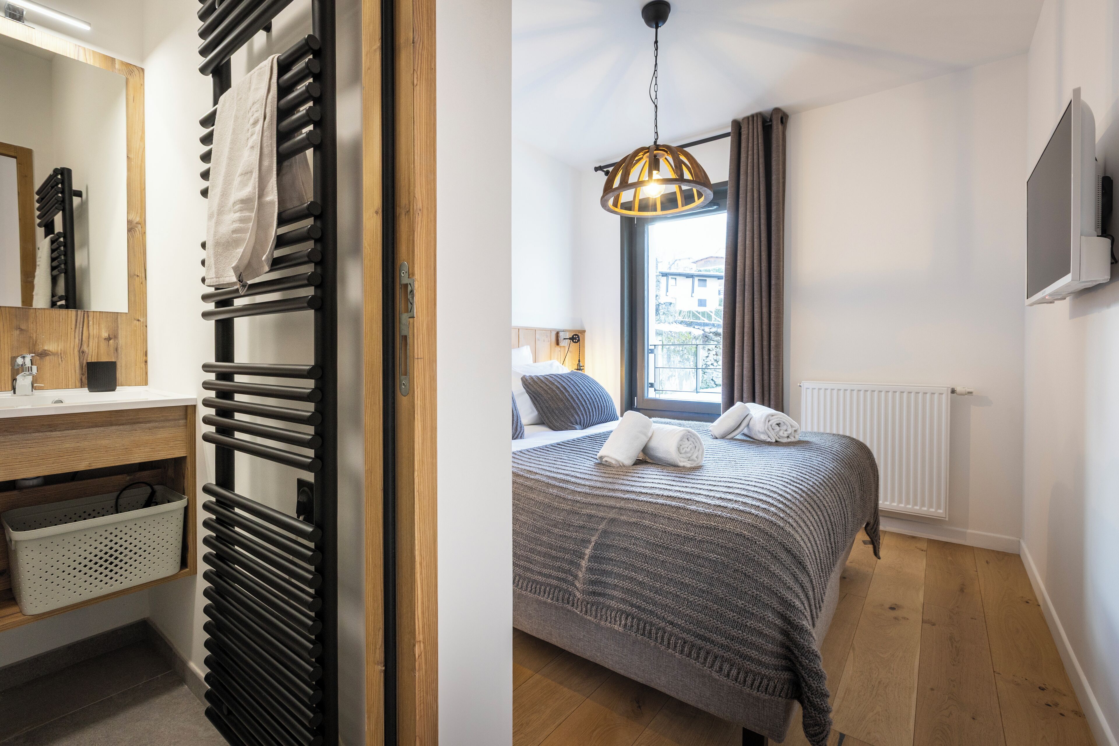 A bedroom with a bed, a window with curtains, a radiator, and a TV on the wall.