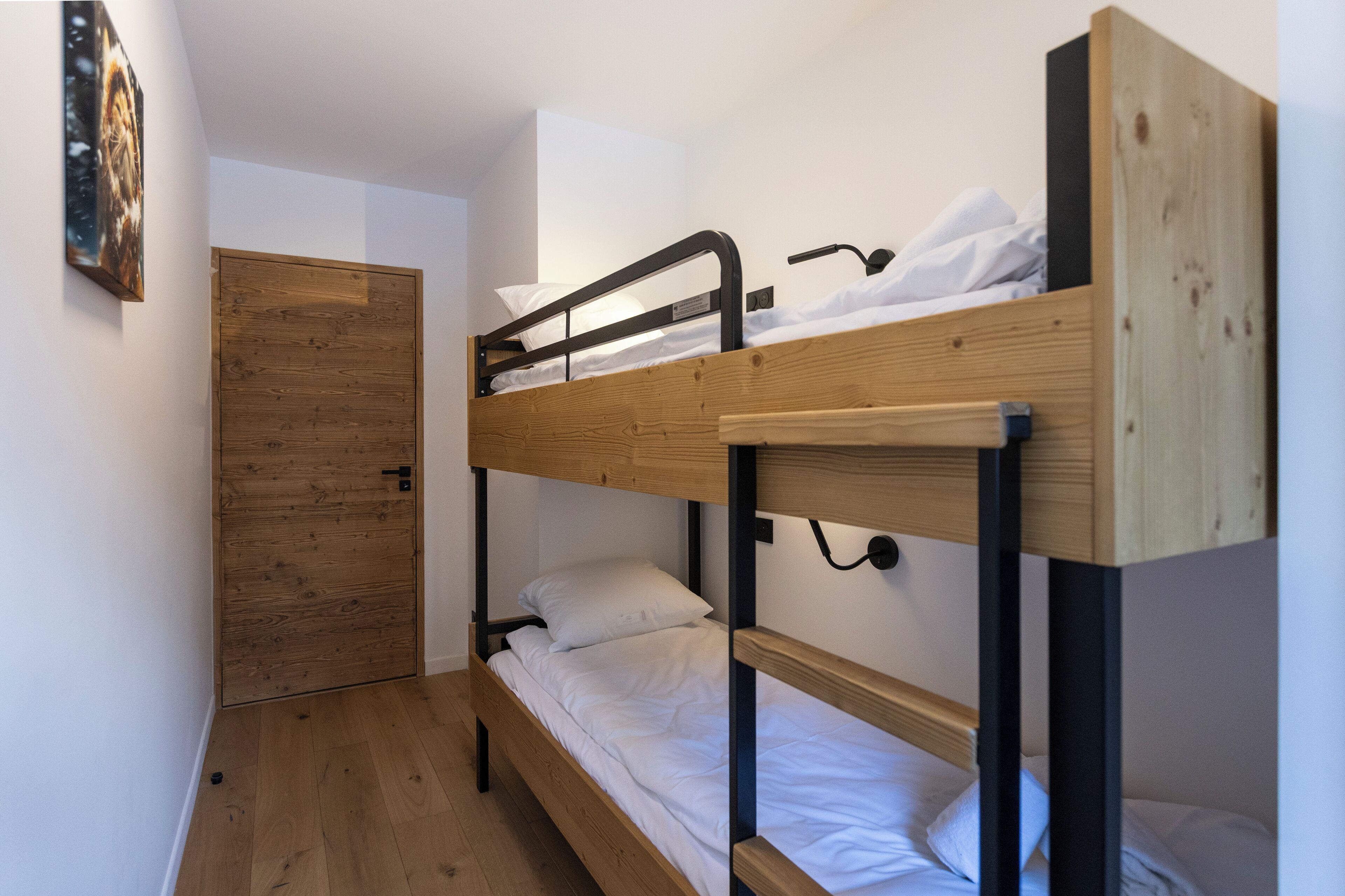 A bunk bed room with a wooden door and a framed picture on the wall.