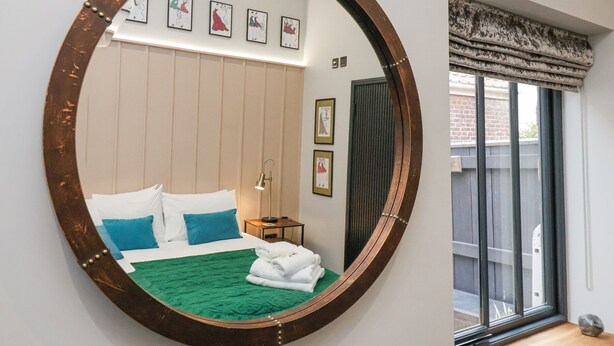 Ein Schlafzimmer mit einem großen, runden Spiegel, einem Bett mit blau-weißer Bettwäsche, einer grünen Decke und einem Nachttisch mit einer Lampe.