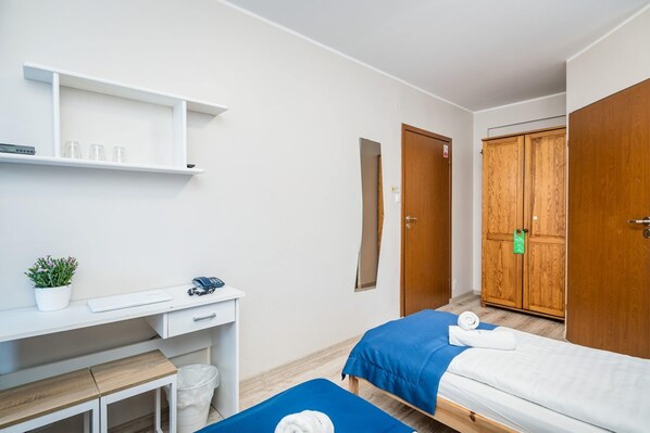 Een hotelkamer met een bureau, twee bedden, een kast en een spiegel.