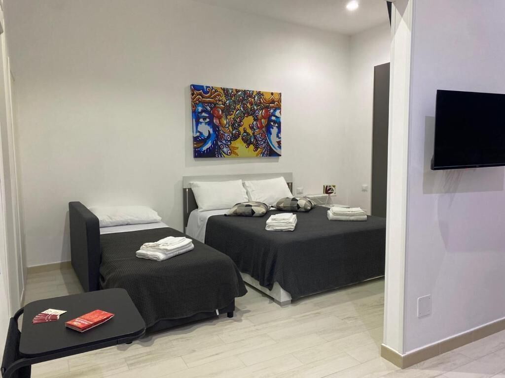 A hotel room with two beds, a flat-screen TV, a painting on the wall, and a small table with books.
