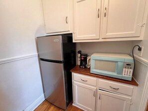 A compact kitchen with a refrigerator, a coffee maker, and a microwave on a wooden countertop.