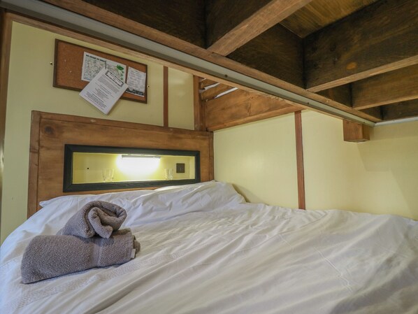 A bed with white linens, a wooden headboard, and a towel on the side. - Betsy (Woodbridge)