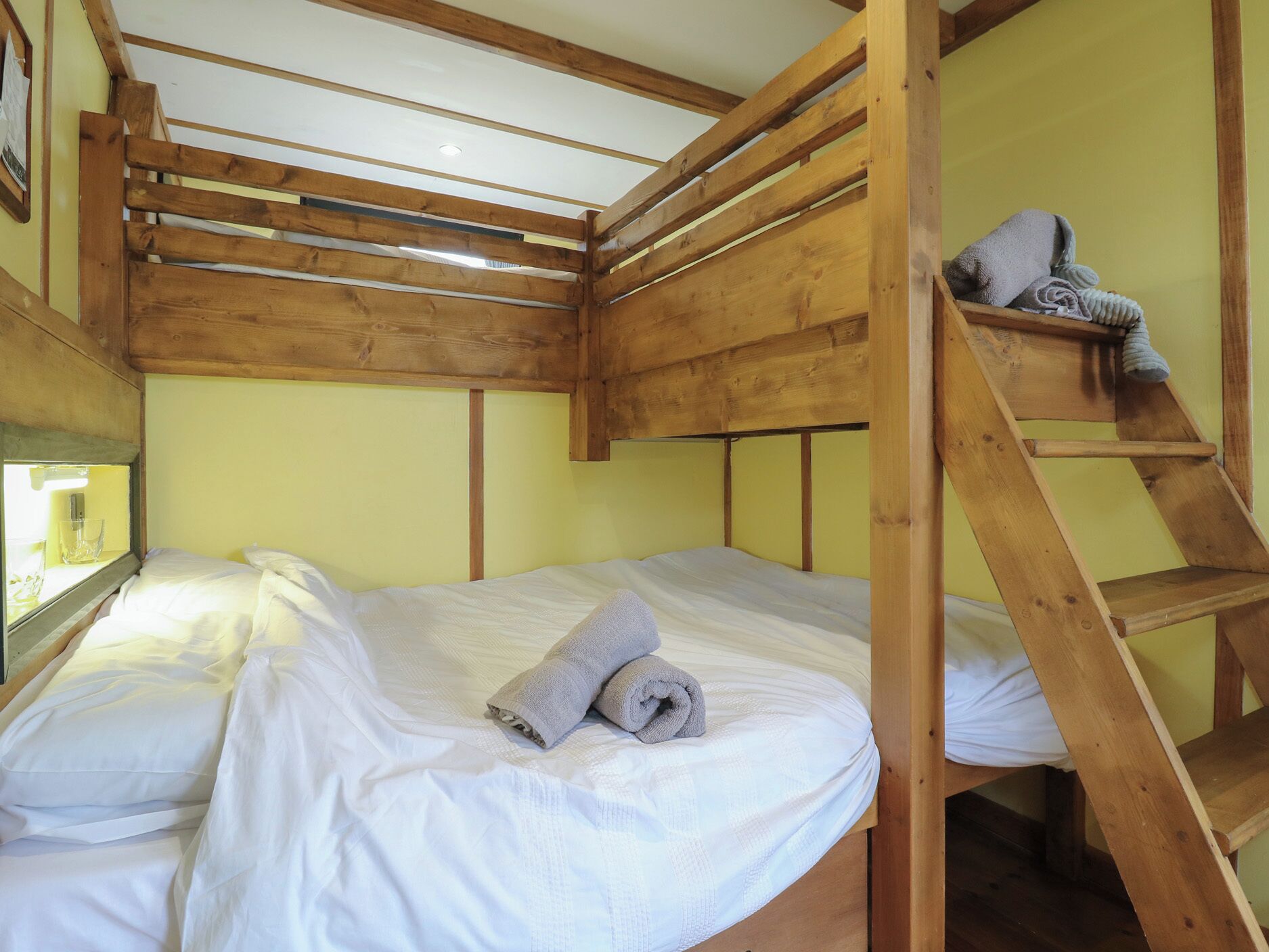 A bunk bed room with wooden beams, a small shelf, and a window with a glass.