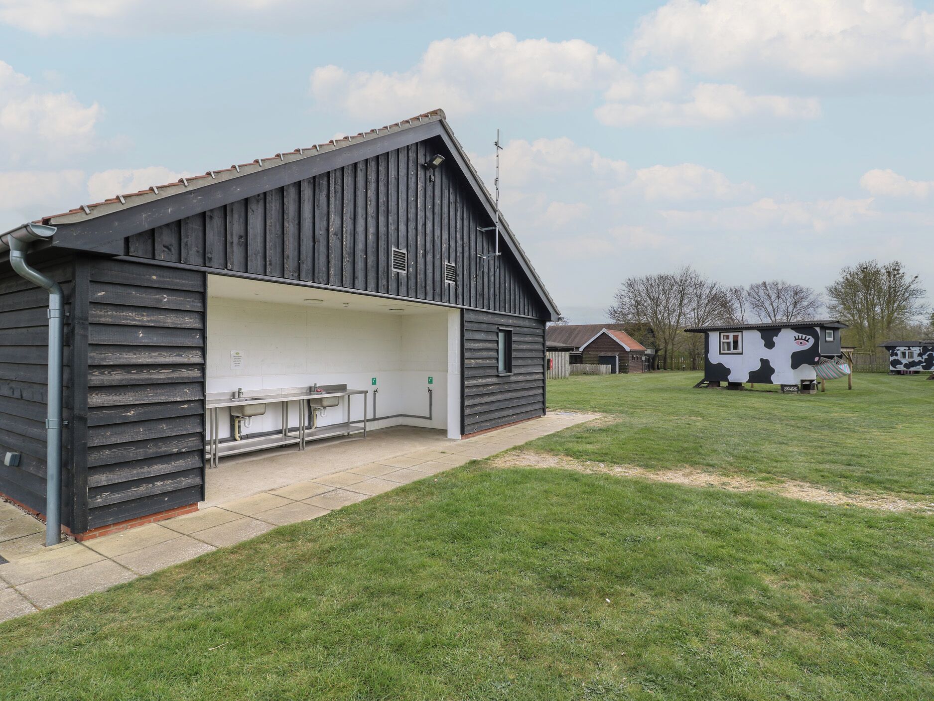 A rustic barn-style building with a covered outdoor seating area and a small cow-themed playhouse in the background.