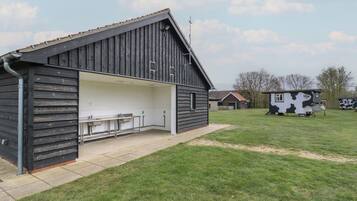 A rustic barn-style building with a covered outdoor seating area and a small cow-themed playhouse in the background.