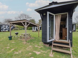 A small, single-room cabin with a sliding door, a wooden porch, and a picnic table. - Betsy (Woodbridge)