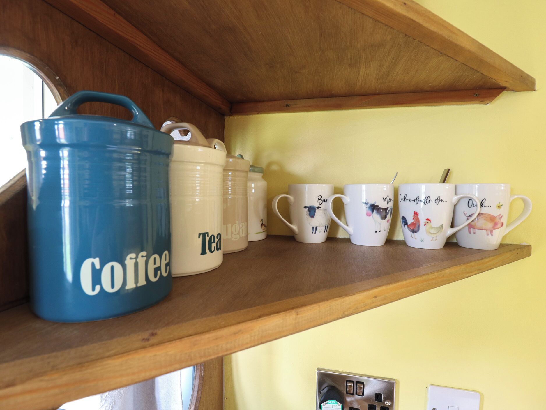 Une étagère contenant divers articles de cuisine, notamment un récipient bleu pour le café, un récipient pour le thé et plusieurs tasses ornées de motifs animaliers.
