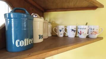 Une étagère contenant divers articles de cuisine, notamment un récipient bleu pour le café, un récipient pour le thé et plusieurs tasses ornées de motifs animaliers.