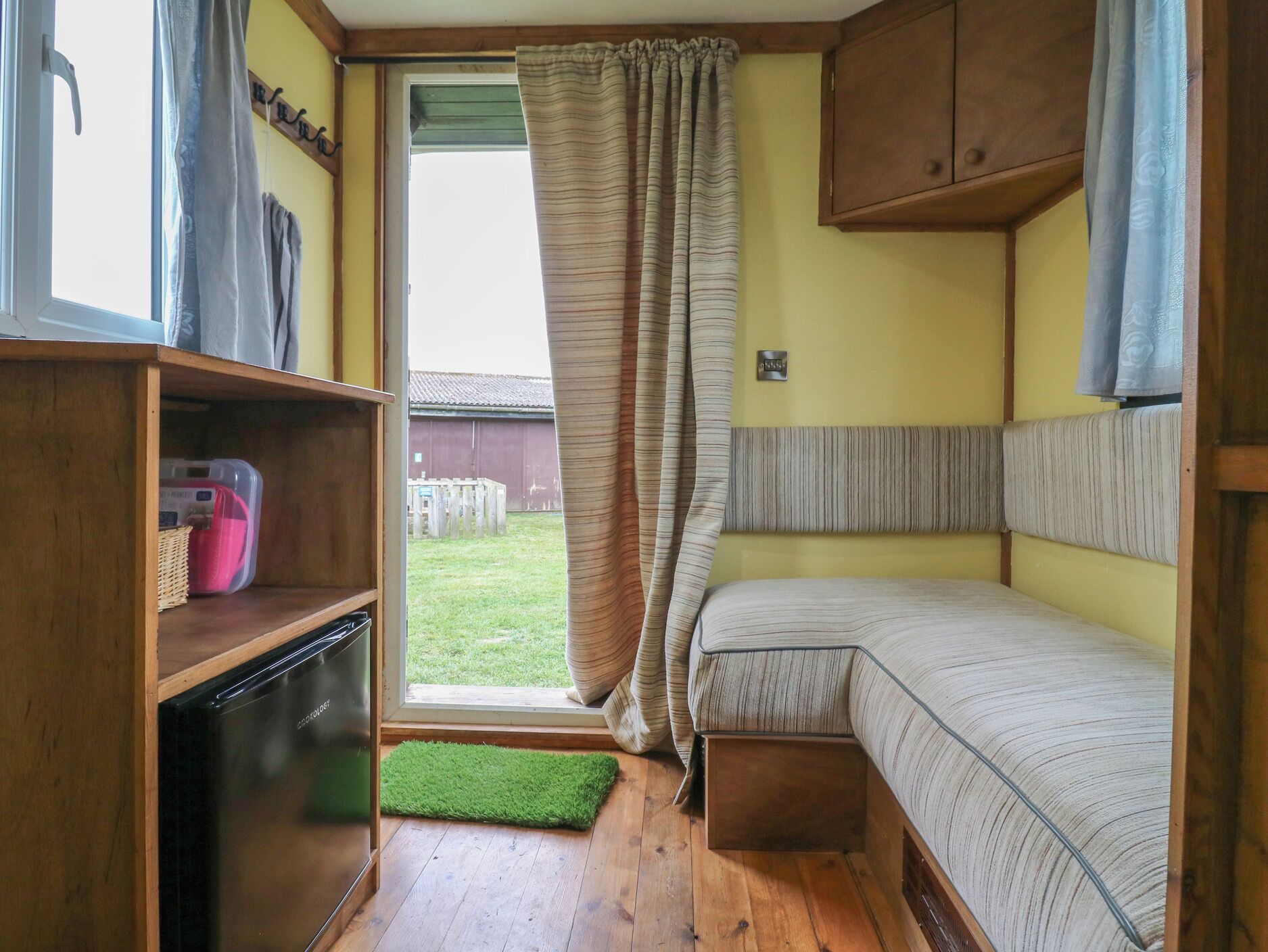A compact room with a bed, a wooden cabinet, a small shelf, and a window with curtains.