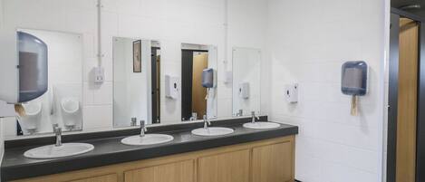 Un lavabo públic amb tres rentabios, armaris de fusta i dispensadors de gel hidroalcohòlic.