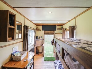 Ein gemütliches Blockhaus-Interieur mit Holzwänden, einem kleinen Schreibtisch mit einer Korb voller Bücher, einem Fenster mit Vorhängen und einem Etagenbett mit gemustertem Bettbezug.