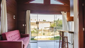 Ein Zimmer mit einem rosa Sofa, einem Esstisch mit einem Stuhl und einem großen Fenster mit Blick auf ein Gebäude und Grünflächen.