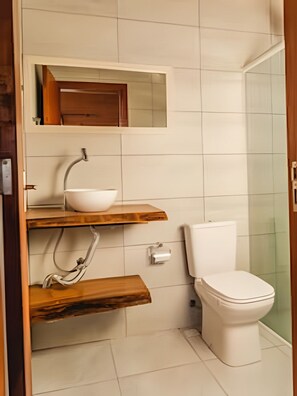 A bathroom with a white toilet, a wooden vanity with a white sink, and a mirror above the sink. - Casa Ibiraquera - Praia do Rosa - SC 2 (Imbituba)