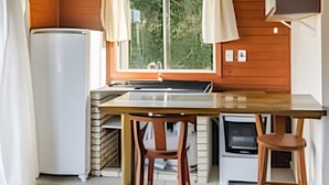 Eine kleine Küche mit Holzboden, einem Fenster mit Vorhängen, einem Kühlschrank, einer Spüle und einem Herd.