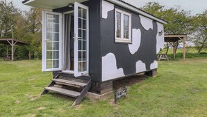 Eine kleine, eingeschossige Holzhütte mit weissem Anstrich und schwarzen Küstenmuster-Akzenten. Sie hat eine Eingangstür mit Fensterfeldern und ein paar Stufen, die zur Haustür führen.