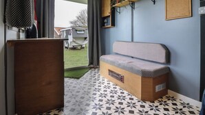Ein gemütlicher Raum mit einer Sitzbank, einem Holzschrank, einer kleinen Ablage mit Pflanzen und Blick ins Freie.