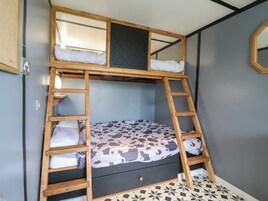 Una cama litera con una escalera, una ventana pequeña y un espejo en la pared.