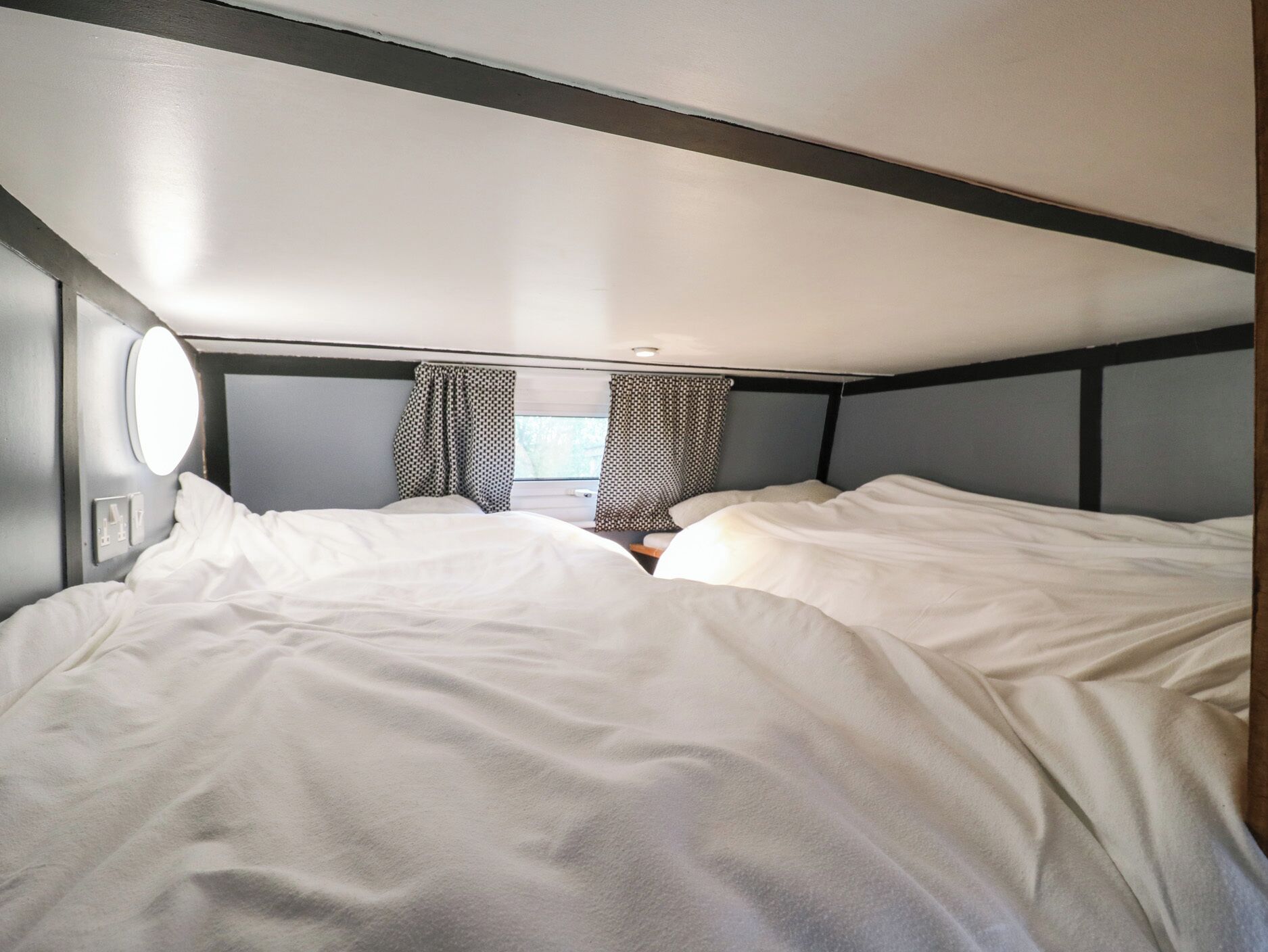 Un dormitorio pequeño con dos camas, una ventana con cortinas y un espejo redondo en la pared.