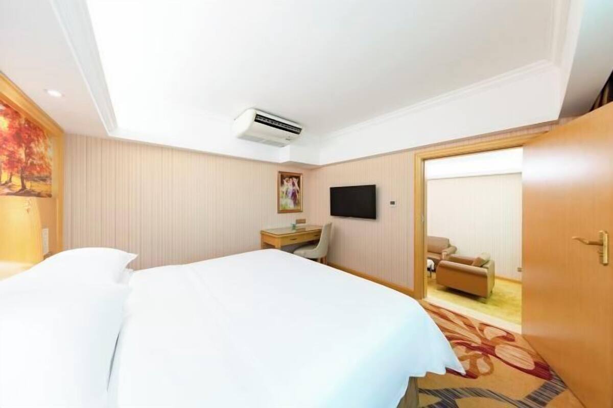 A hotel room with a bed, a desk, a chair, a television, and an air conditioning unit.