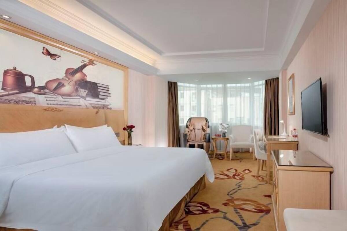 A hotel room with a large bed, a desk, a television, and a mural on the wall.
