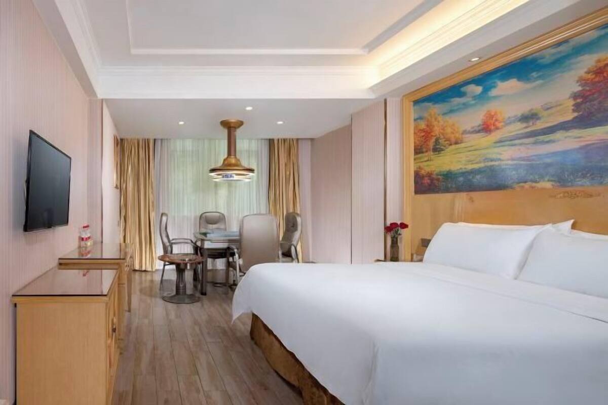 A hotel room with a bed, a desk, a chair, a television, and a painting on the wall.