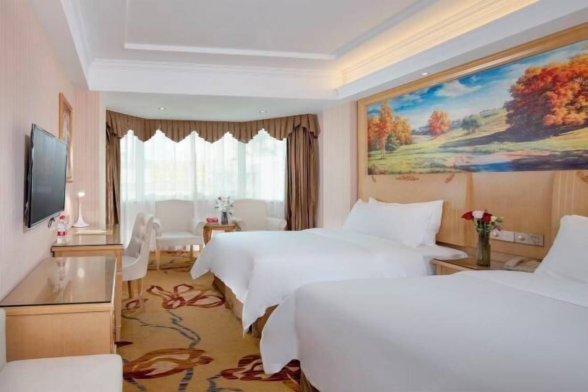 A hotel room with two beds, a TV, a desk, and a painting on the wall.