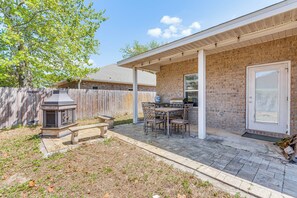 Une terrasse à l’arrière de la maison, avec une maison en briques, une clôture en bois, un barbecue et un banc en pierre.