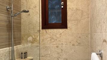 A shower area with a glass door, a towel rack, and a shelf with toiletries.