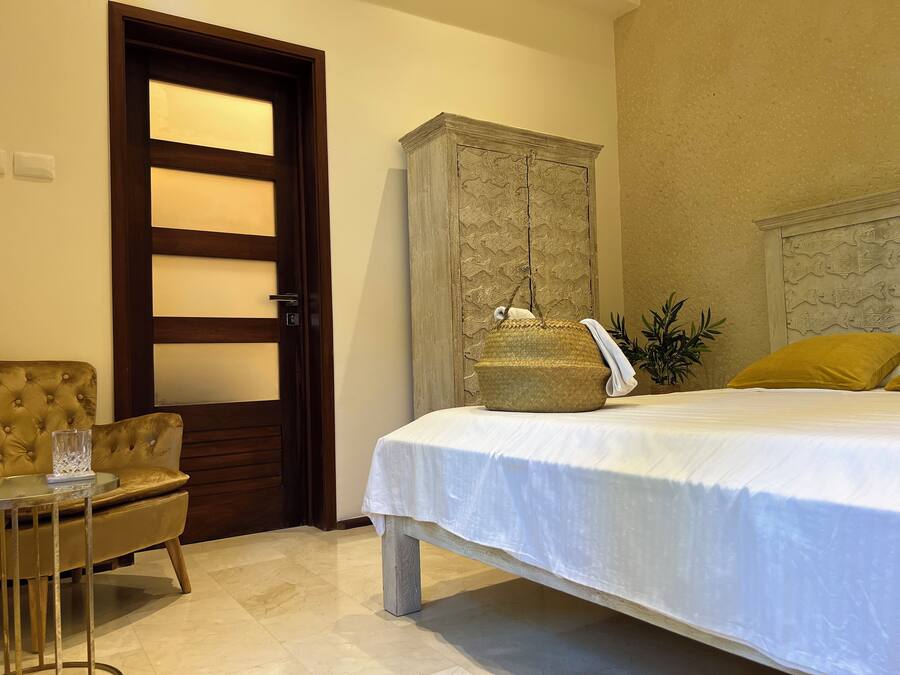 Een slaapkamer met een bed, een houten kledingkast, een stoel en een klein tafeltje met een glas.