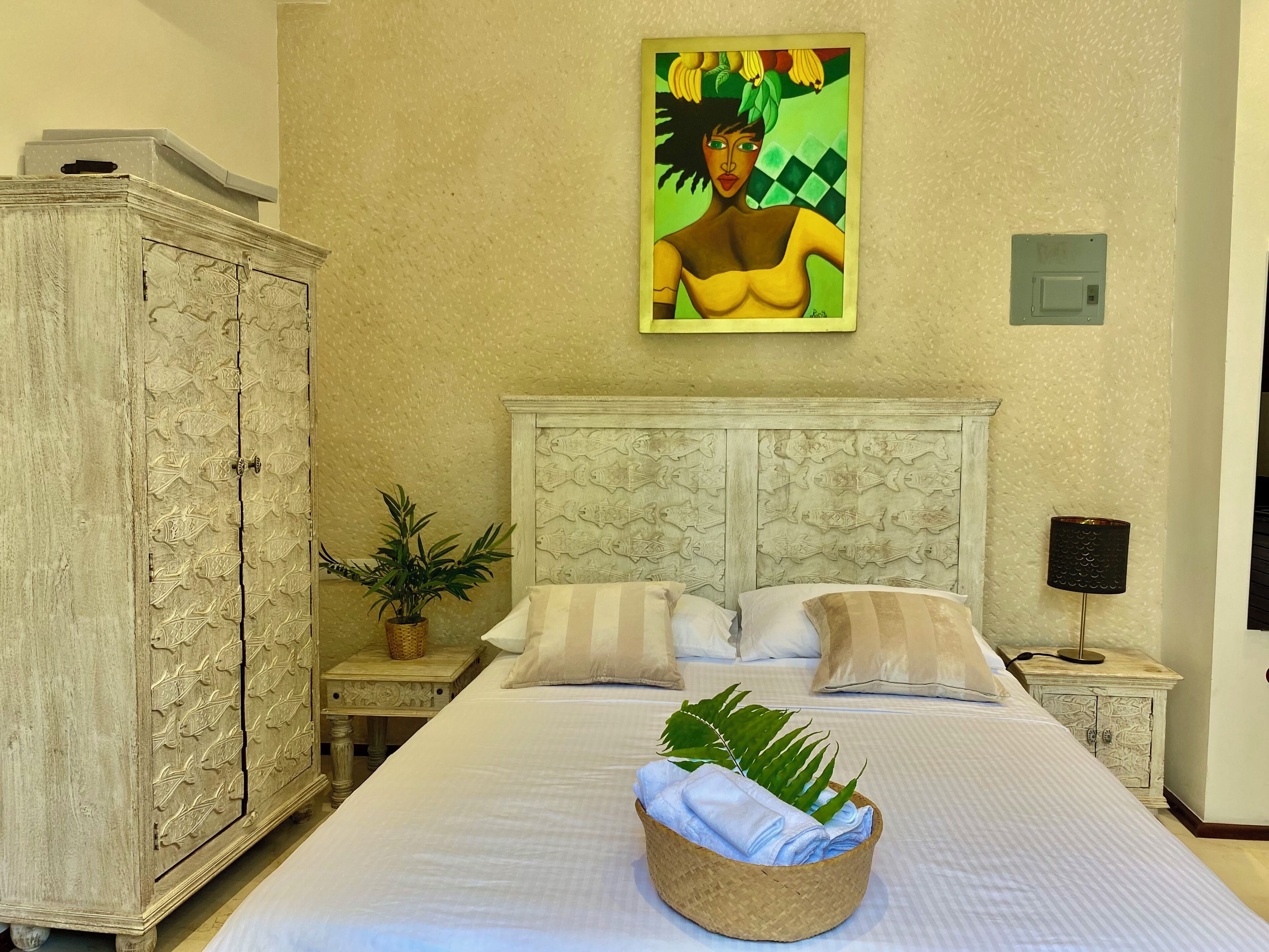 A bedroom with a bed, pillows, a nightstand, a lamp, a painting, and a cabinet.