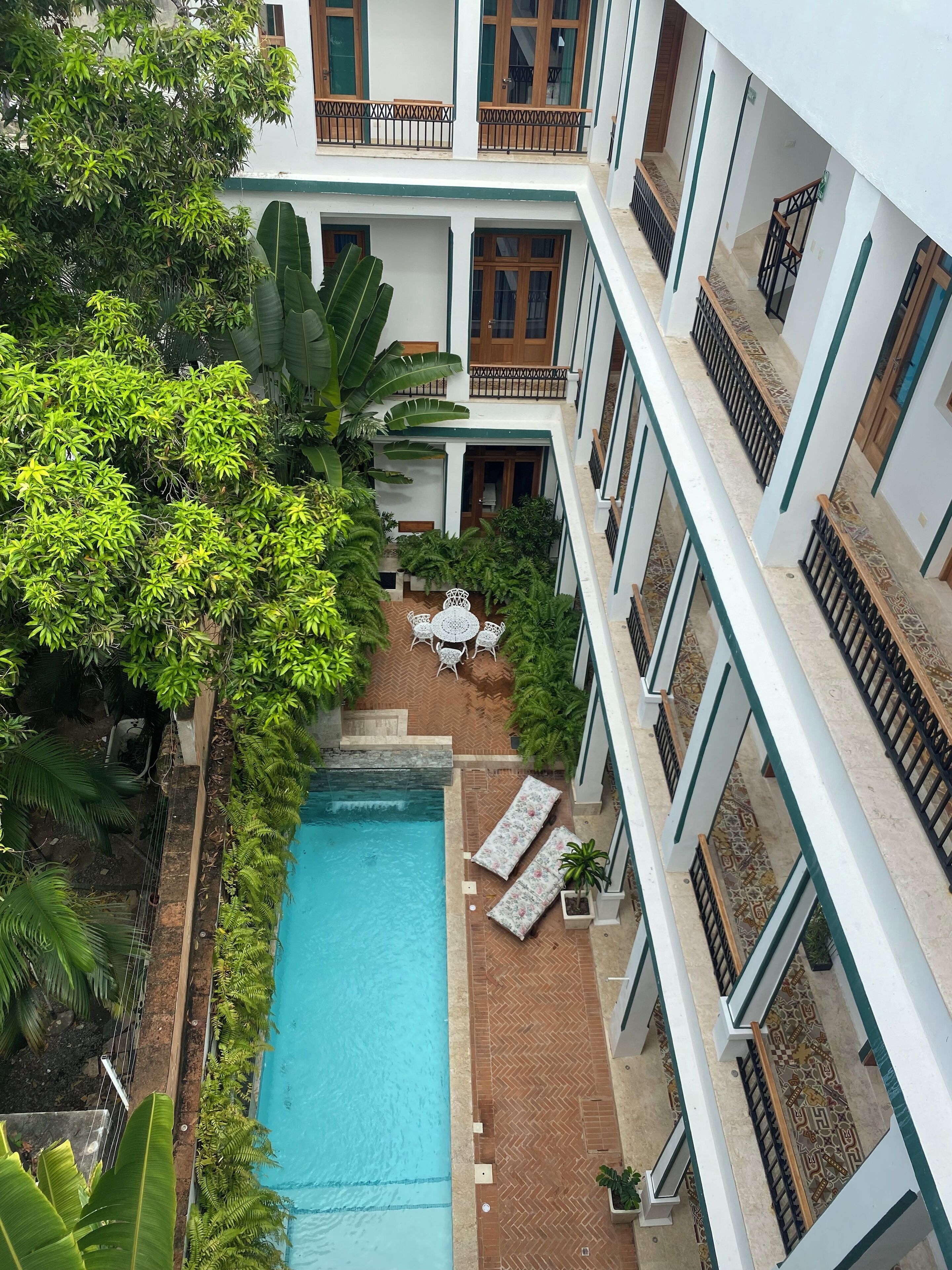 A multi-level hotel with a central swimming pool, surrounded by lush greenery and outdoor seating areas.