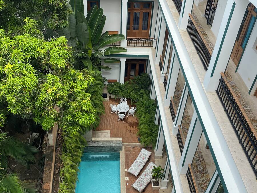 A multi-level hotel with a central swimming pool, surrounded by lush greenery and outdoor seating areas.