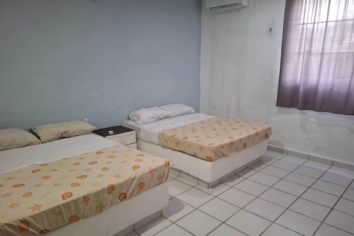 A room with two beds, a small table, and a window with curtains.