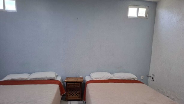 Una habitación de hotel pequeña y sencilla con dos camas, una mesita de noche de madera y una ventana.