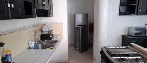 A kitchen with a sink, stove, refrigerator, and cabinets.