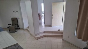Ein geräumiger Raum mit gefliestem Boden, einer Treppe, die zu einer Tür führt, und einem Sessel in der Ecke.
