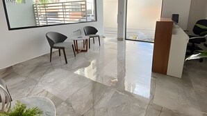 A modern office space with a reception desk, two chairs, a small table, and a large window with a view of buildings and trees. - City Center Apartment Torre Leonardo VI (Santo Domingo)
