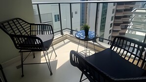 A balcony with two black chairs and a small table, a potted plant, and a view of modern buildings. - City Center Apartment Torre Leonardo VI (Santo Domingo)