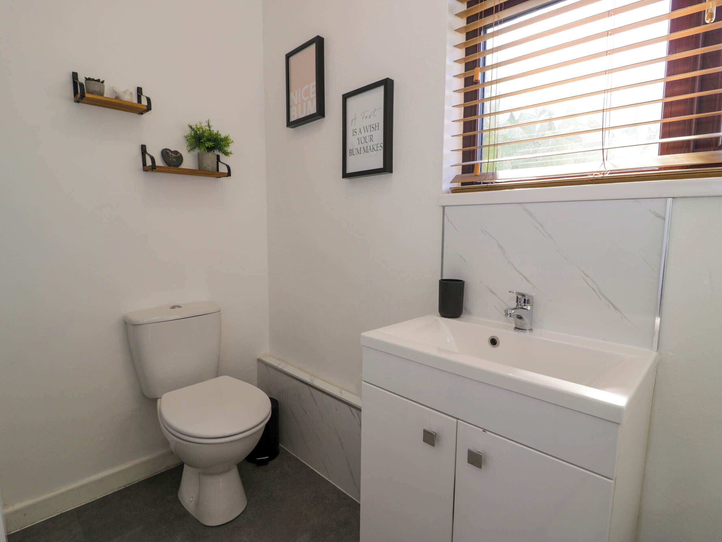Une salle de bain moderne équipée de toilettes, d’un lavabo et d’une fenêtre avec des stores.