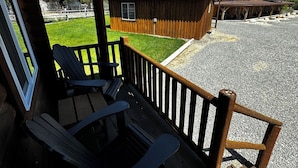 Una terraza de madera con dos sillas Adirondack, un camino de grava y una construcción rústica con techo de metal.