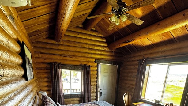 Un dormitorio tipo cabaña de madera con una cama, escritorio, silla y ventilador de techo.